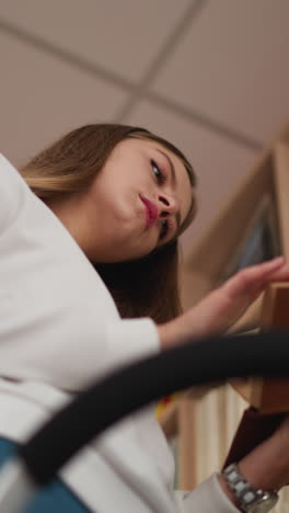 young woman chooses book from upper shelf. focused female student peruses book searching literature for scientific project. college library premise