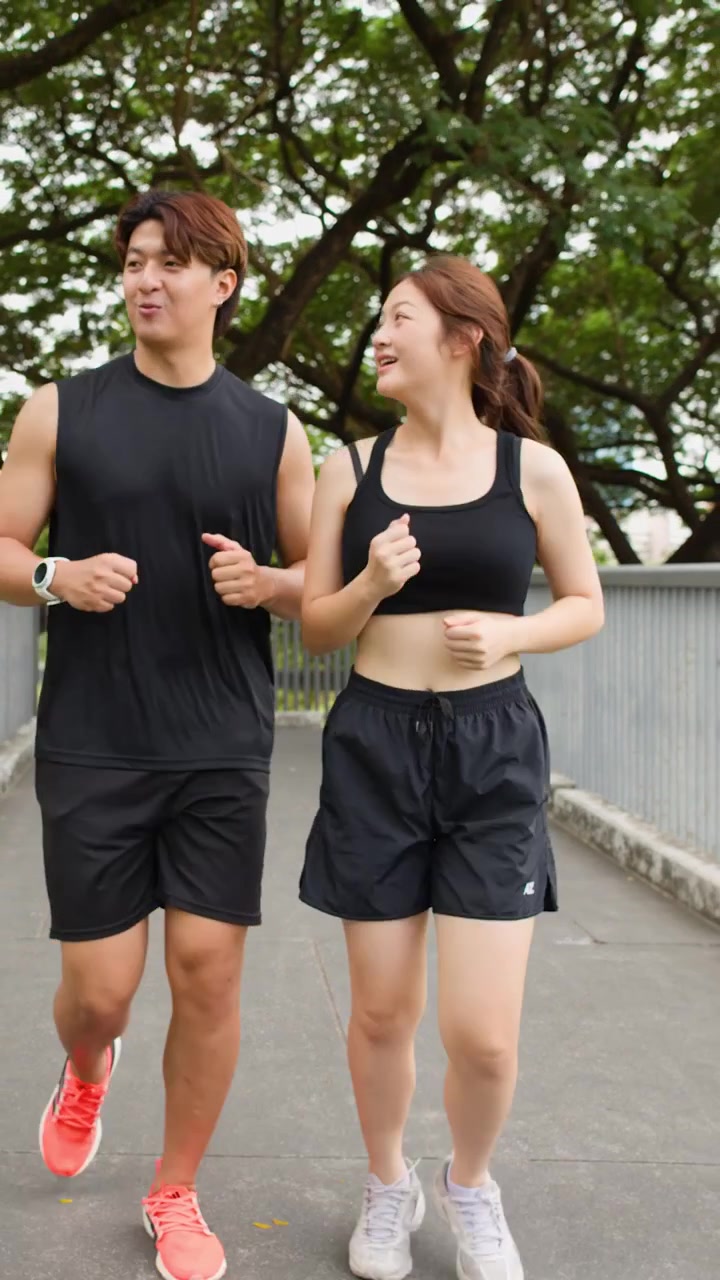 Giovane uomo e donna asiatici che fanno jogging insieme su un ponte alberato alla luce del mattino.