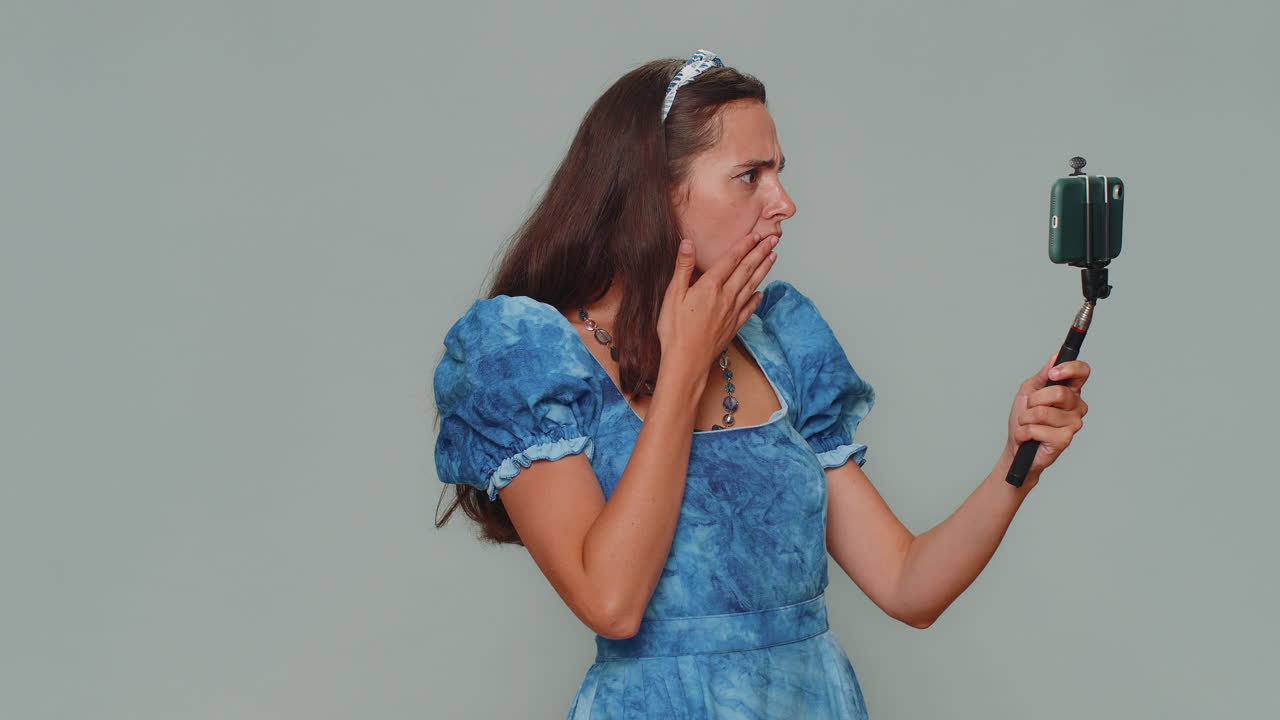 mujer blogger impresionada tomando selfie en el teléfono móvil selfie stick, comunicando llamada de video en línea
