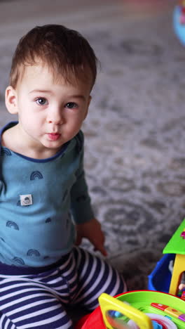 cute caucasian toddler playing with toys on the floor. kid presses button on the toy and watches it working. top view. vertical video
