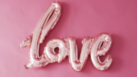 Rack-focus-video-of-shiny-pale-pink-love-text-balloon,-on-pink-background-with-copy-space