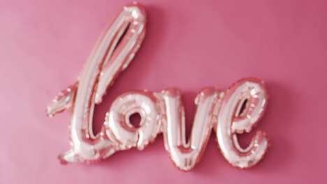 rack focus video of shiny pale pink love text balloon, on pink background with copy space