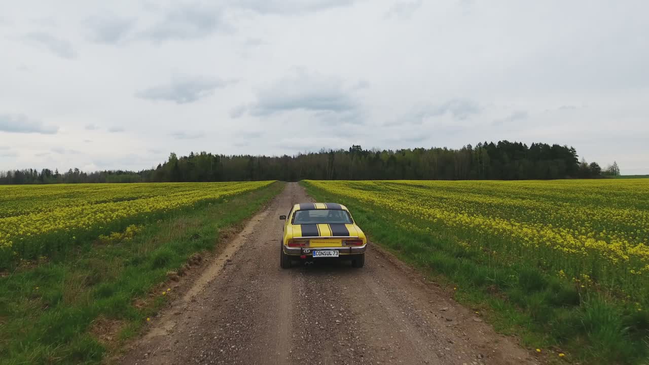 Yellow With Black Stripes Classic Ford Consul Rides On A Gravel Road. 4K Aerial Footage