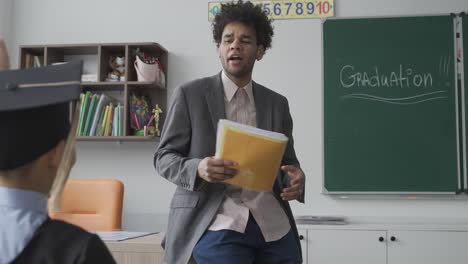 grupo de felices estudiantes de preescolar multirraciales con birrete y bata. están sentados y escuchando a su maestro.