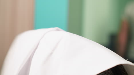 close-up view of a lab chair's backrest with a scientist's arm holding a white lab coat in the background, preparing to putting it on the chair and walking away