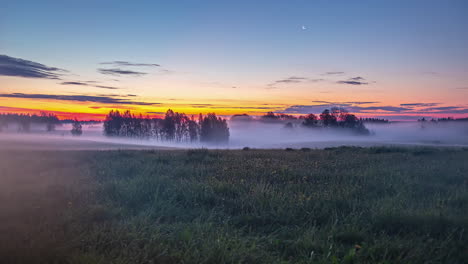 wide timelapse of mist moving by grass field and trees at twilight