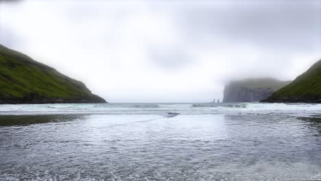 Sea-water-reaching-shore-of-Tjörnuvik-beach---low-level-shot-with-view-of-Risin-and-Kellingin-in-background-during-cloudy-day-on-Streymoy-Island,-Faroe-Islands