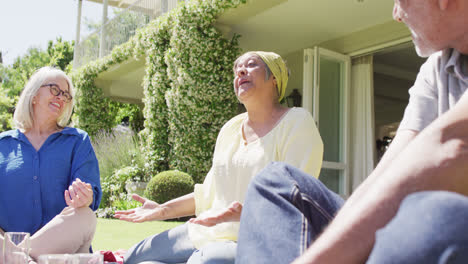 Happy-biracial-senior-woman-talking-with-diverse-friends-at-a-picnic-in-sunny-garden,-slow-motion