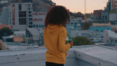 happy african american woman with afro hairtyle dancing on rooftop enjoying weekend  looking at beautiful city skyline at sunset