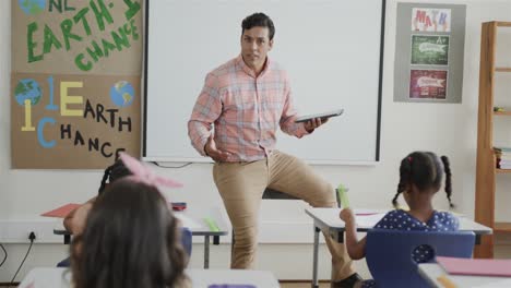 diverse children at desks and male teacher using tablet in elementary school class, slow motion