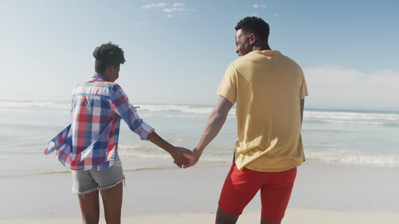 Rear view of african american couple holding hands walking on the beach