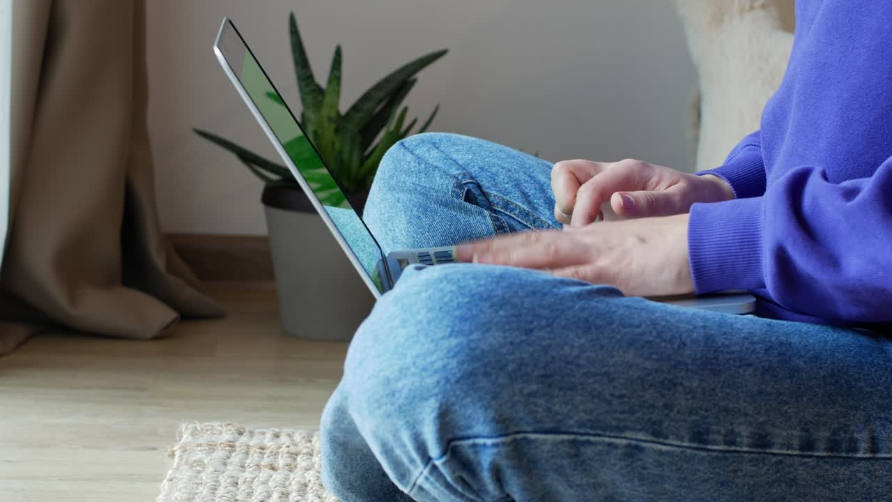 A girl sitting in front of the window on the floor, working on her laptop.