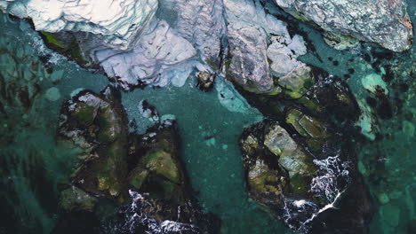 bird's eye view pan follows ocean waves crashing on white rocky shoreline