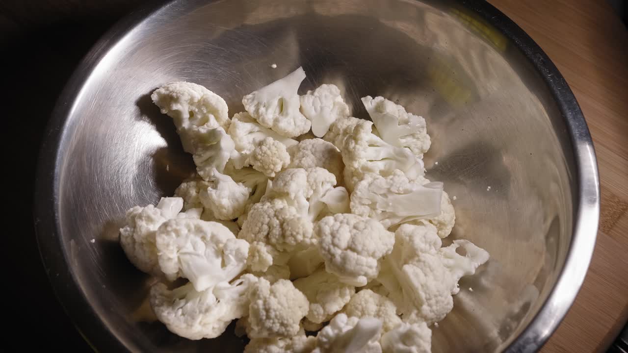 생 콜리플라워를 금속 그릇에 추가하고 구운 콜리플라워를 요리하는 사람 - 스테디 샷