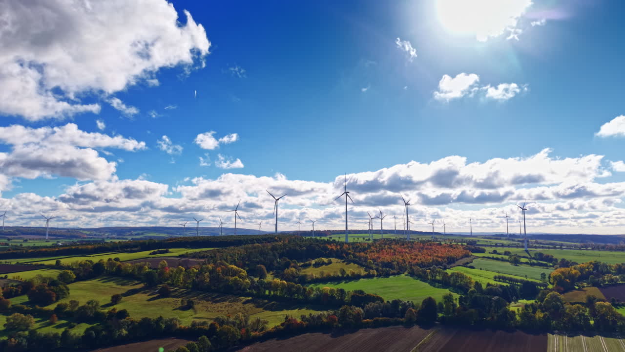 Turbine eoliche ruotano con eleganza in un paesaggio pittoresco sotto un cielo blu brillante con nuvole soffici a mezzogiorno