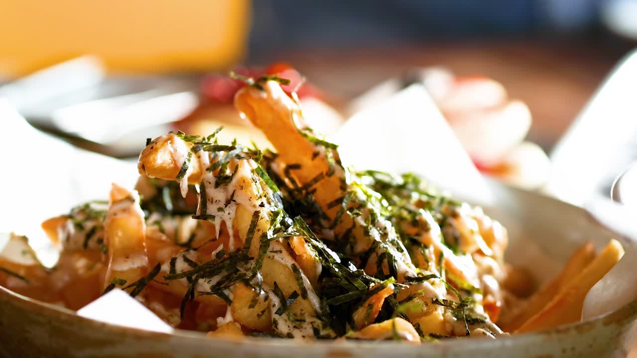 A close-up view of crispy French fries topped with herbs and sauce, served in a paper-lined bowl.