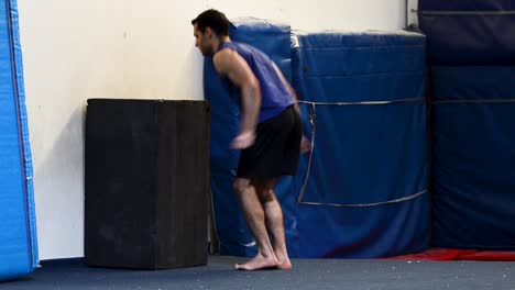 a still shot of a guy in a gymnastics gym doing high jumps to a box from a back view