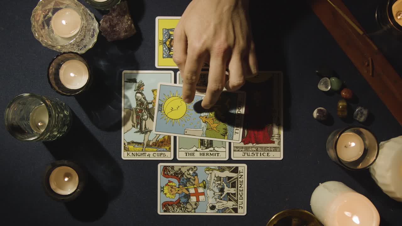 toma aérea de una persona que hace una lectura de cartas del tarot colocando cartas en la mesa con velas y cristales 1