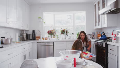 Excited-young-girl-and-her-mum-put-cakes-in-the-oven-while-baking-together-in-the-kitchen,-close-up