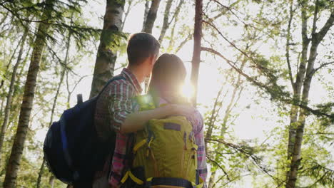 A-Young-Couple-Of-Tourists-Enjoy-A-Walk-In-The-Woods-At-Sunset-They-Stand-Hug-And-Look-Forward-Back-