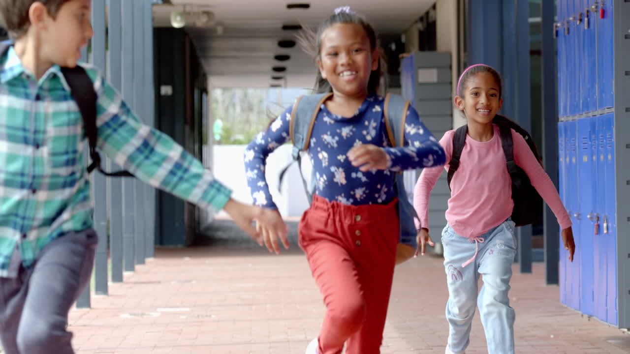 In school, three young biracial students running in hallway