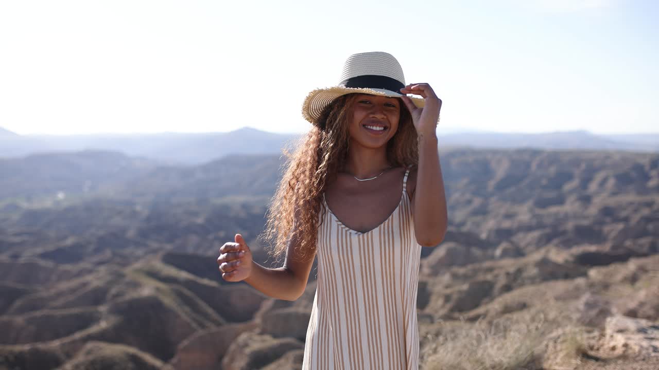 Young woman in a striped dress and hat enjoying a scenic desert landscape