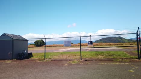 Gimbal-wide-shot-from-a-moving-vehicle-approaching-a-chain-link-fence-in-front-of-a-small-helicopter-at-a-heliport-on-the-island-of-Kaua'i-in-Hawai'i