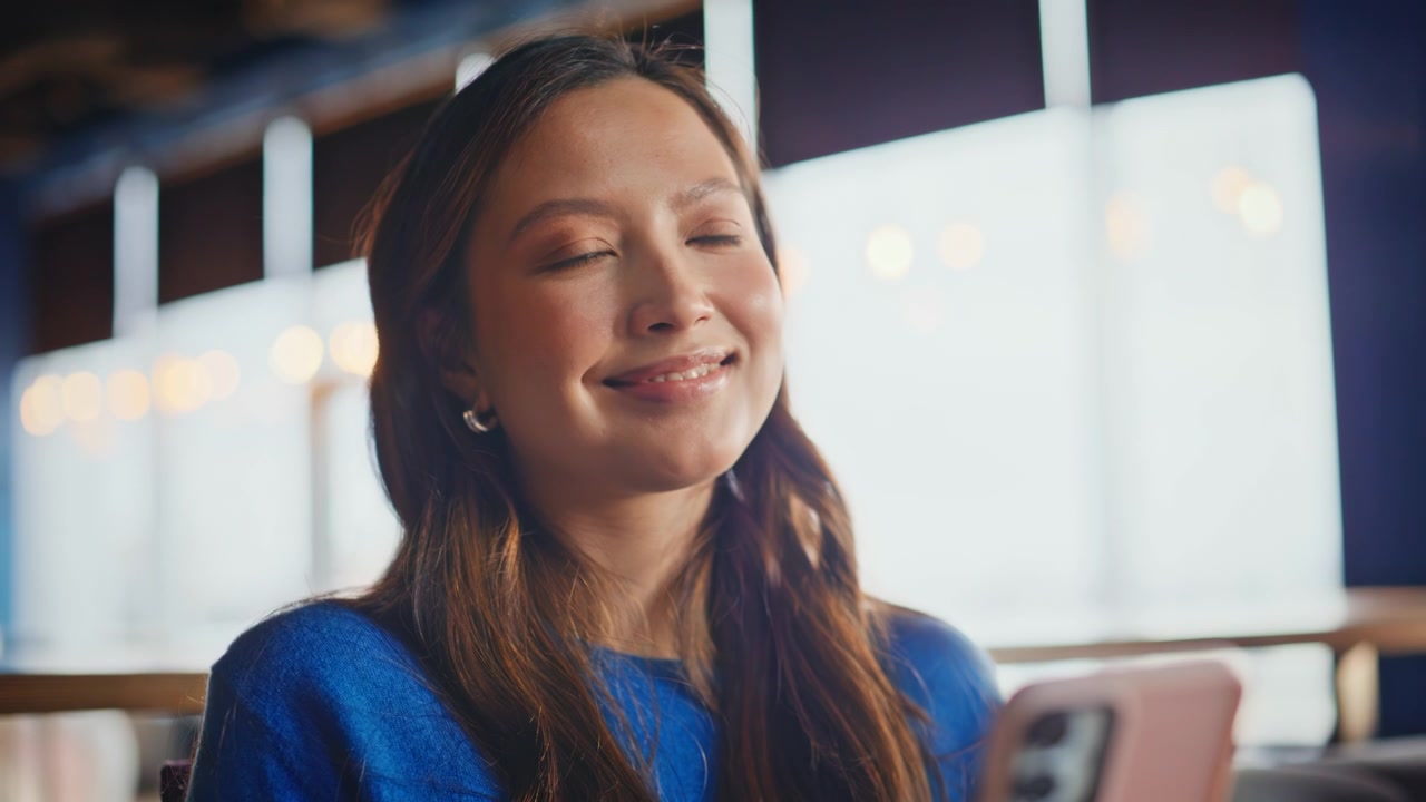 カフェでスマートフォンを操作するアジア人女性。携帯電話を使う幸せそうな女性のクローズアップ