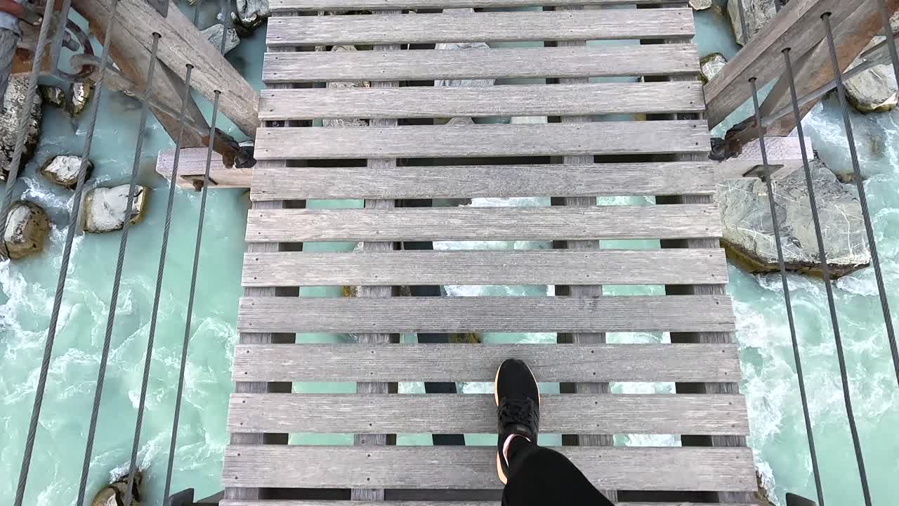 POV Looking down while walking along a bridge on the Hooker Valley Trail, New Zealand. You can see the blue rushuing water between the slats of the bridge
