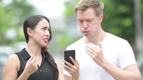 young multi-ethnic couple using phone together in the streets outdoors