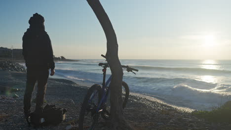 a solitary man stands on a gravel beach, watching the sunrise over the sea