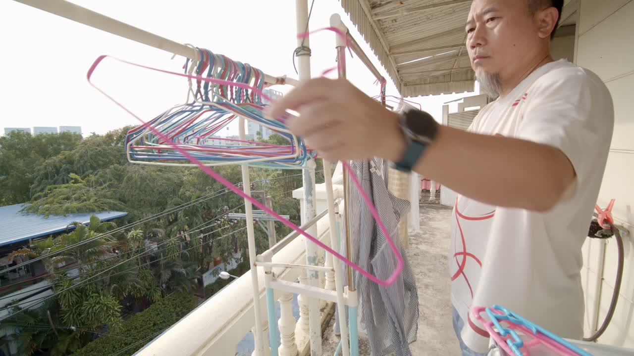 Asiatisk mann som henger opp klær til tørk på balkongen sin - saktefilm
