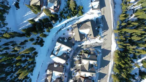 overhead shot of peaceful snowy condos in big sky, montana, nestled among pine forests, with winding snowy paths and mountain peaks in the distance—ideal for a cozy winter stay in the woods