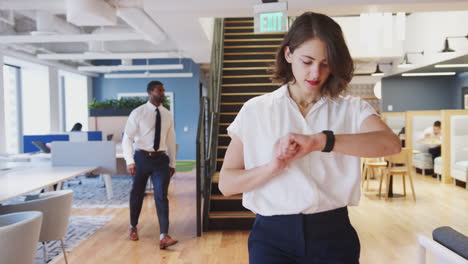 businesswoman walking through modern office checking data on smart watch