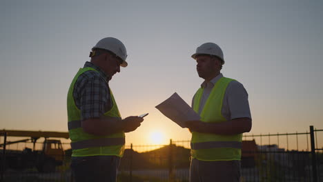 construction manager and workers shaking hands on construction site. builder man with a tablet and a man inspector in white helmets shake hands at sunset standing. symbol of agreement successful work.