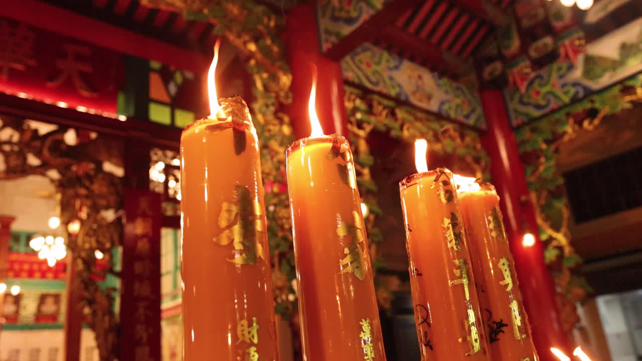Tall candles burn steadily in colorful temple, warm lighting, slight camera movement, spiritual atmosphere