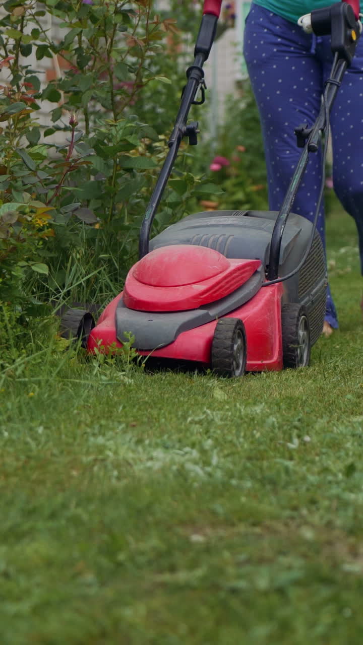 Woman running with a lawn mower in the garden. Close-up. Vertical video