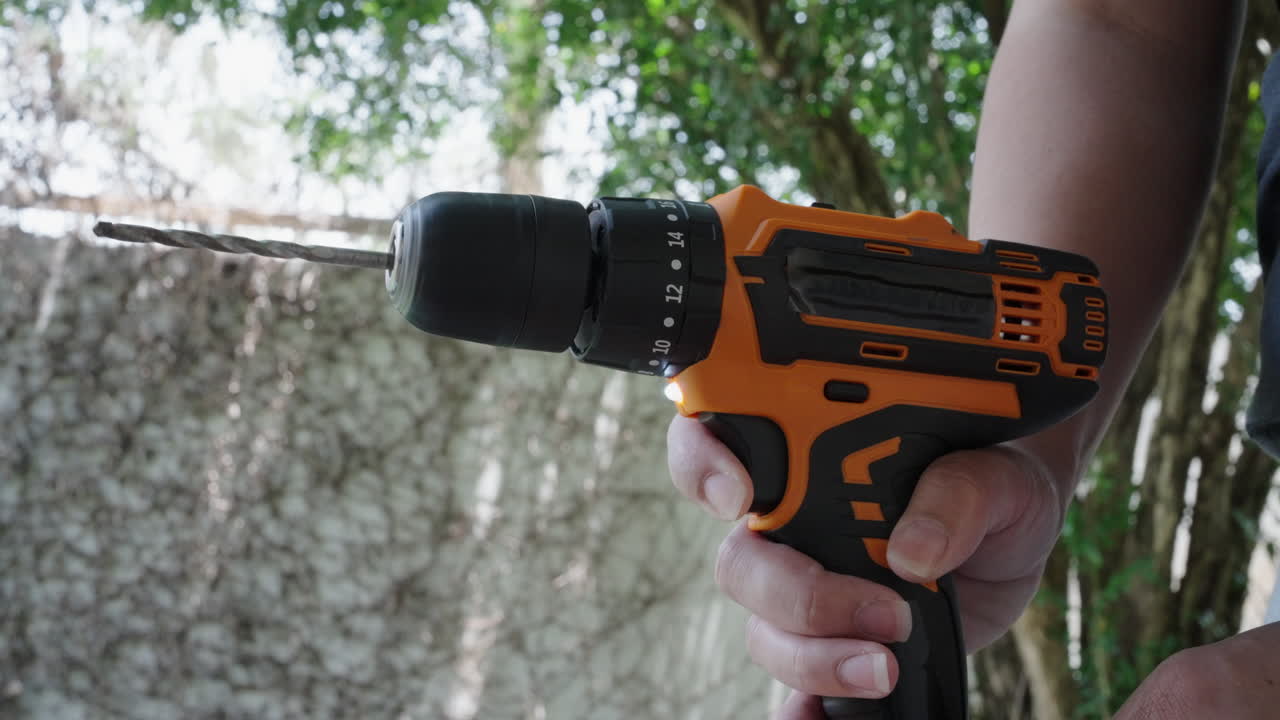 A woman tests a cordless drill trigger outside with close hand detail and bright natural light