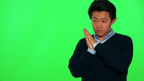 a young asian man sleeps with the head on his hands which are clasped together, then he wakes up and stretches - green screen studio