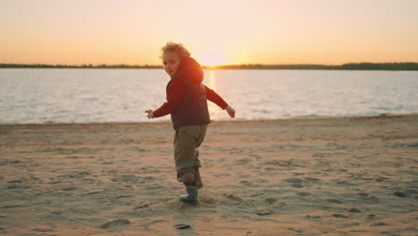 smiling little boy is running on beach in sunset time having fun in nature