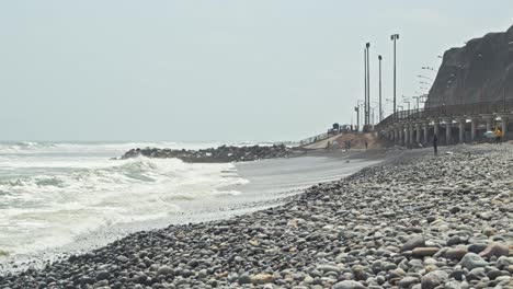 Rounded-rock-beach-with-surfers-and-ice-cream-man-in-Costa-Verde-Lima,-Peru-4k