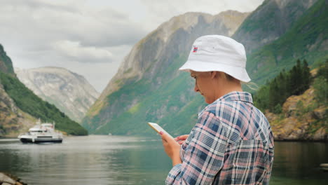 A-Tourist-Uses-A-Smartphone-On-The-Background-Of-The-Picturesque-Norwegian-Fjord-In-The-Distance-A-C