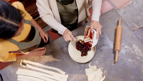 multiracial grandma and young woman preparing cherry pie together in cozy kitchen, at home