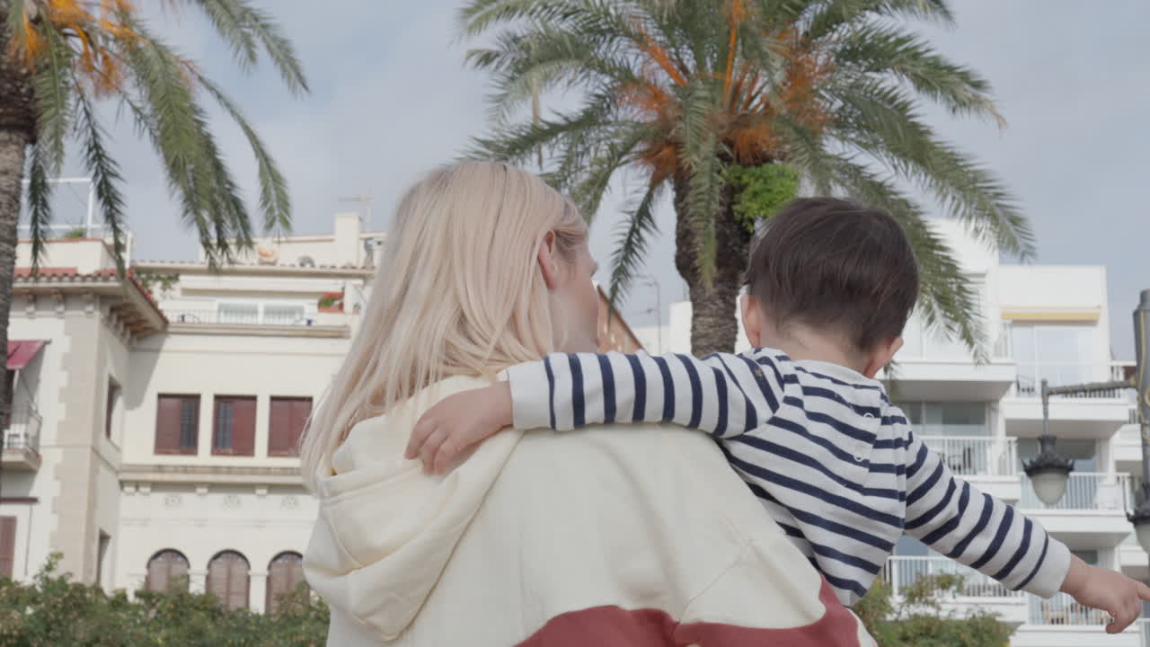 Boy and mom walking laughing and enjoying family time, while exploring city background with palm trees
