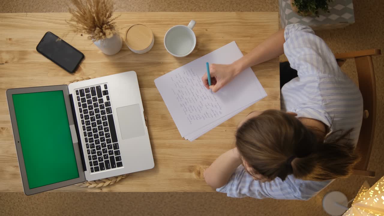 The girl writes down the main points from the conference. A laptop with a green screen. Top view. Remote work and training via the Internet. Take a break for a glass of water