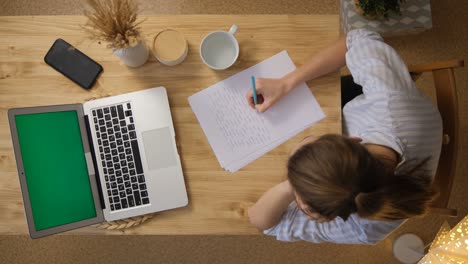 the girl writes down the main points from the conference. a laptop with a green screen. top view. remote work and training via the internet. take a break for a glass of water