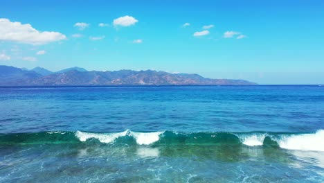 Beautiful-view-of-a-shallow-wave-breaking-and-crashing-against-the-shore-and-scenic-mountains-and-cloudy-sky-in-the-background