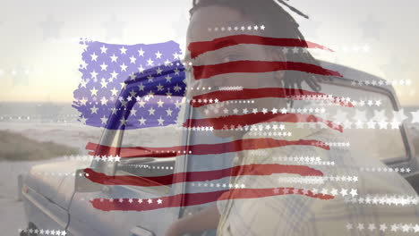 animation of american flag and stars over happy african american man by car on sunny beach