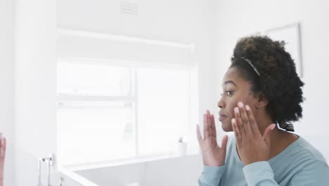 African-american-woman-checking-her-skin,-looking-at-face-in-bathroom-mirror,-slow-motion