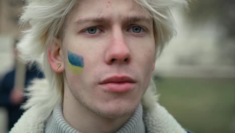 Close-up-portrait-of-young-caucasian-man-with-Ukrainian-flag-painted-on-his-cheek.